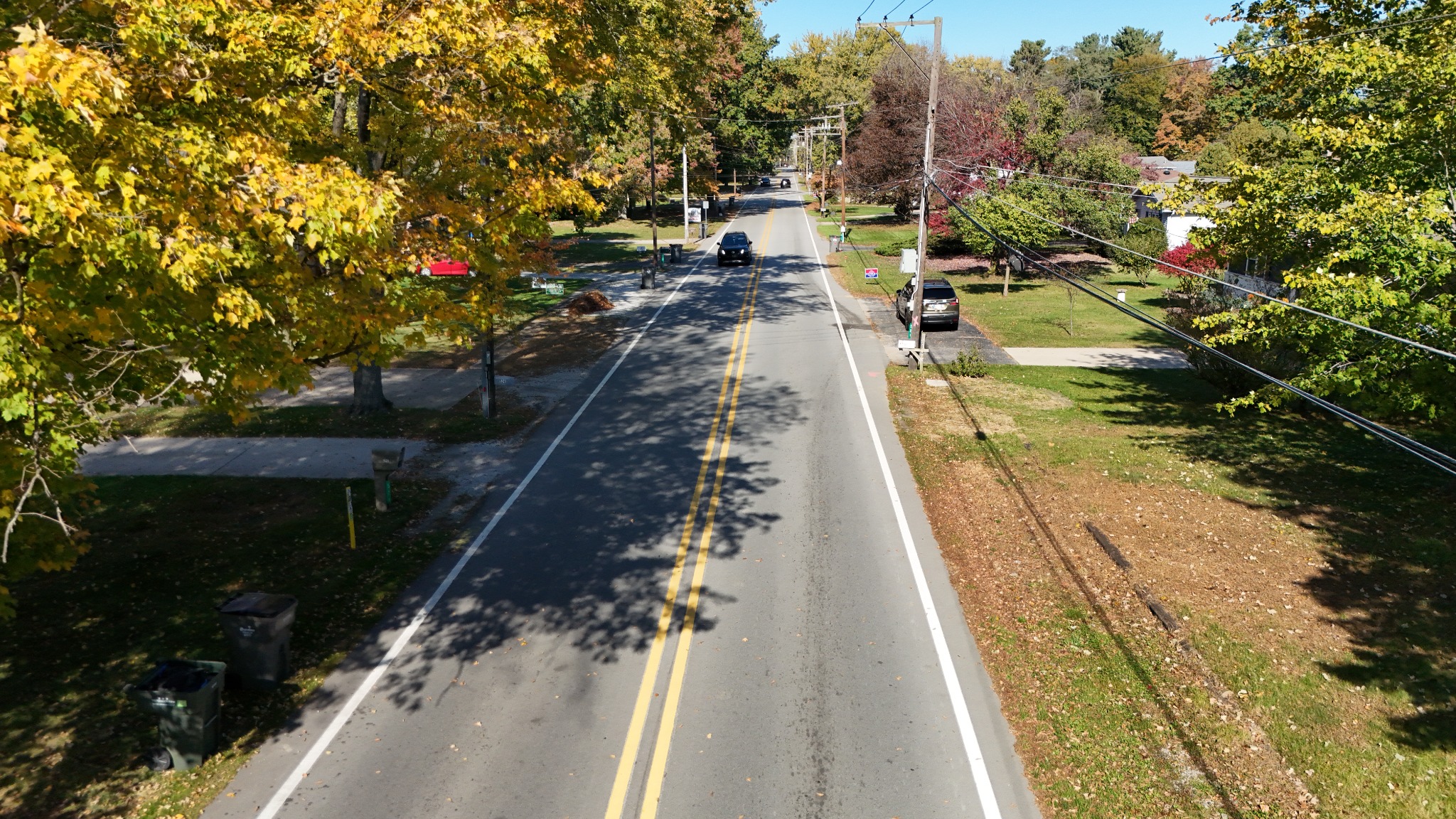 Low aerial view along Johnson Road in Trail Creek, showing pavement markings and the tree-lined residential corridor · October 23, 2026